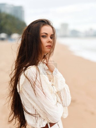 Téléchargez les photos : Femme blanche élégante, seule sur la plage, posant avec élégance calme et magnifiques cheveux rouges, embrassant la lumière d'été et la sensualité dans un fond de nature à la mode - en image libre de droit