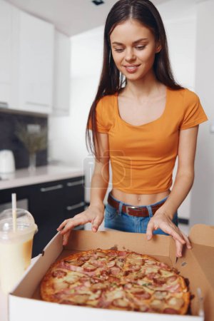 Foto de Mujer con camisa naranja sosteniendo caja de pizza con bebida delante de ella, lista para disfrutar de deliciosa comida en el camino - Imagen libre de derechos