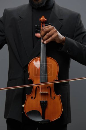 Photo for Elegant African American man in formal attire holding a violin against a neutral gray background - Royalty Free Image