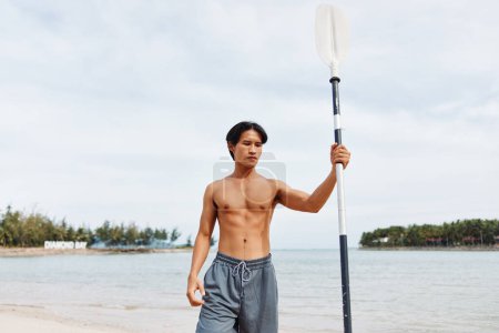 Téléchargez les photos : Homme asiatique actif pagaie à travers les plaisirs d'été sur une plage, embrassant l'aventure océanique - en image libre de droit