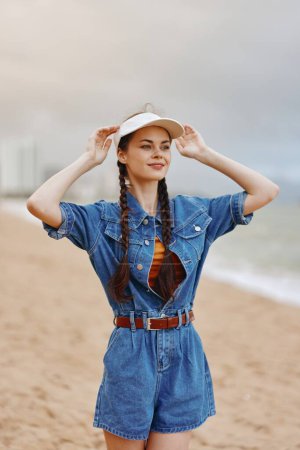 Téléchargez les photos : Beauté en natures Chapeau : Jeune femme séduisante se relaxant au bord de la mer ensoleillée, modelée à la mode dans une jolie robe sur fond de plage tropicale - en image libre de droit