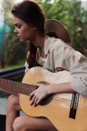 Téléchargez les photos : Une femme joue de la guitare acoustique devant une piscine en chemise blanche - en image libre de droit