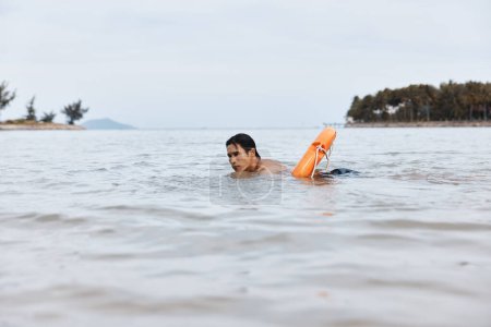 Téléchargez les photos : Gardien de la joie estivale : Un sauveteur asiatique sur une plage, sauvant les nageurs avec une bouée de sauvetage dans un océan bleu vibrant - en image libre de droit