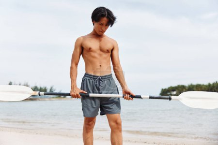 Téléchargez les photos : Homme asiatique actif profitant d'une aventure SUP estivale amusante sur la plage - en image libre de droit