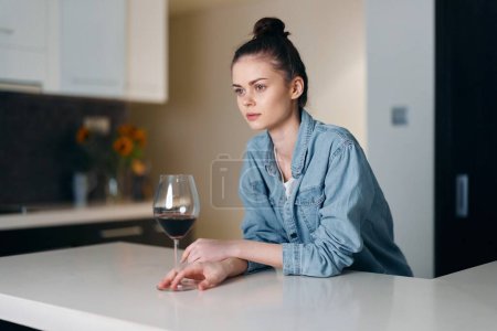 Foto de Mujer triste y solitaria bebiendo vino sola: retrato de una dama desesperada en la cocina blanca. - Imagen libre de derechos