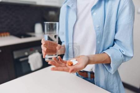 Foto de Mujer que toma medicamentos y se mantiene hidratada en la cocina con un vaso de agua y una pastilla en la mano - Imagen libre de derechos