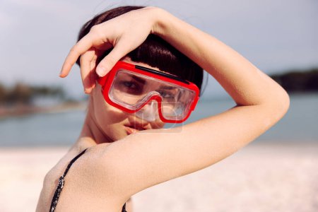 Téléchargez les photos : Joyeuse femme plongée avec tuba en maillot de bain rouge, souriant à la caméra sur fond de plage tropicale - en image libre de droit