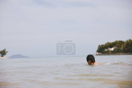 Téléchargez les photos : Homme asiatique souriant nageant dans l'océan bleu tropical : Vacances Béatitude - en image libre de droit