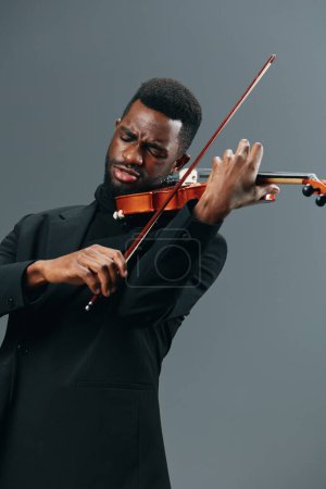 Téléchargez les photos : Élégant homme afro-américain en costume noir se produisant sur violon sur fond gris - en image libre de droit