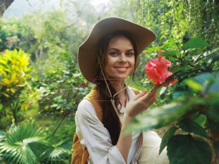 Téléchargez les photos : Une femme dans un chapeau tient une fleur dans sa main tout en se tenant au milieu d'un jardin - en image libre de droit