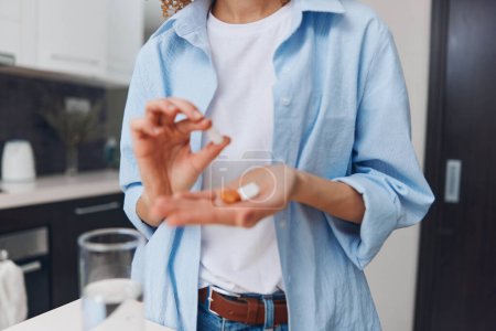 Photo for Woman holding pill standing in front of glass of water ready to take medication for health treatment - Royalty Free Image