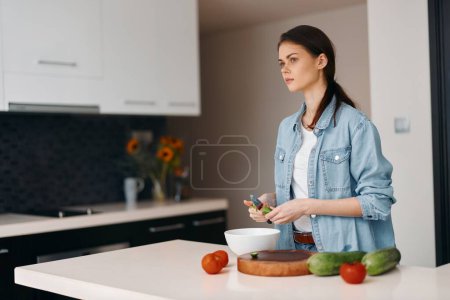 Téléchargez les photos : Jeune chef saine debout dans une cuisine, préparant une salade végétarienne fraîche sur une table - en image libre de droit
