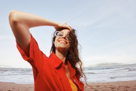 Téléchargez les photos : Femme souriante avec des lunettes de soleil, Faire place à la liberté, Profiter du coucher de soleil coloré à la plage - en image libre de droit
