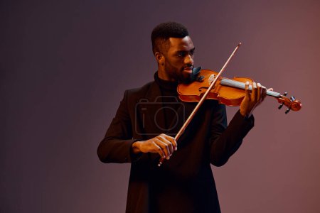 Téléchargez les photos : Afro-Américain en costume jouant élégamment du violon dans un éclairage dramatique sur fond sombre - en image libre de droit