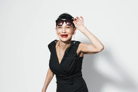 Foto de Mujer elegante con lápiz labial rojo posando en vestido negro delante de la pared blanca para la sesión de fotos de retrato de cámara - Imagen libre de derechos