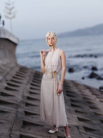 Téléchargez les photos : Natures Glamour : Un jeune modèle féminin attrayant posant sur une pierre de plage, fuyant l'élégance et le style sous le soleil d'automne, avec un fond océanique fascinant - en image libre de droit