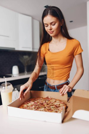 Photo for Woman in orange shirt enjoying delicious slice of pizza straight from the cardboard box - Royalty Free Image