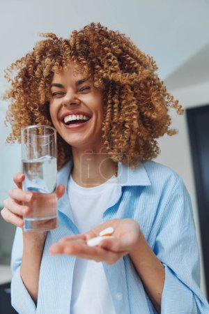 Woman with curly hair holding glass of water and pill in hand, healthcare and medication concept