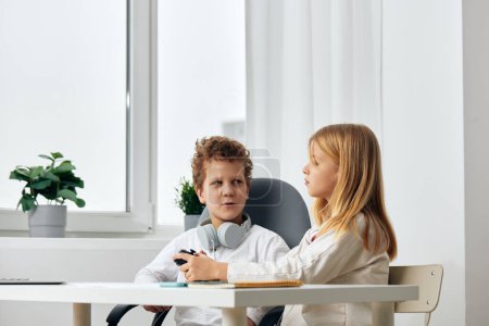Photo for Happy Caucasian Boy and Girl Studying at Home with Laptops Description Two cheerful children, a boy and a girl, are sitting at a table in a cozy living room, engrossed in their online learning - Royalty Free Image