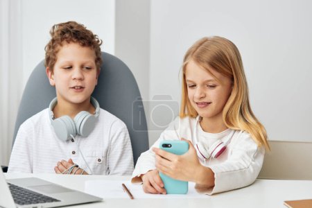 Foto de Niños felices estudiando en casa usando computadoras portátiles y tabletas para elearning, sentados en una mesa en su acogedora sala de estar El niño y la niña, totalmente concentrados, están conectados a Internet, vistiendo - Imagen libre de derechos