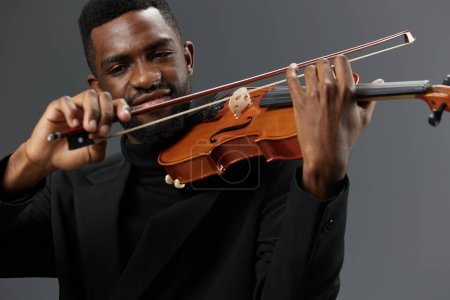 Téléchargez les photos : Un talentueux musicien afro-américain en costume noir élégant jouant du violon sur un fond gris neutre - en image libre de droit