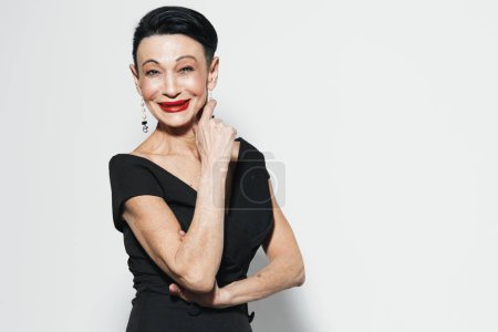 Elegant mature woman in stylish black dress and bold red lipstick posing gracefully against white background
