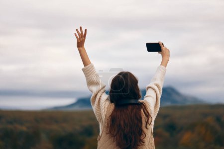 Mountain Adventurer: A Smiling Woman on a Nature Hiking Trip, Taking a Selfie with her Smartphone in the Beautiful Outdoor Landscape