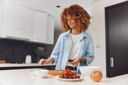 Foto de Mujer afroamericana joven cocinando comida saludable en la cocina moderna en casa, preparando ingredientes frescos para la cena - Imagen libre de derechos