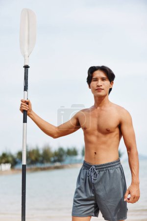 Homme asiatique actif jouissant de sports nautiques d'été sur une planche à pagaie au coucher du soleil sur une plage