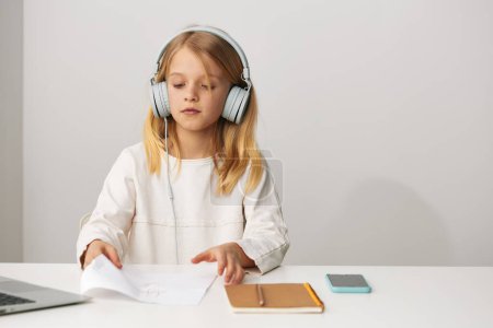 Photo for Happy young girl using a laptop for elearning and online games at home, enhancing her education and digital skills With a smile on her face, she sits at a table with notebooks and a writing notebook, - Royalty Free Image