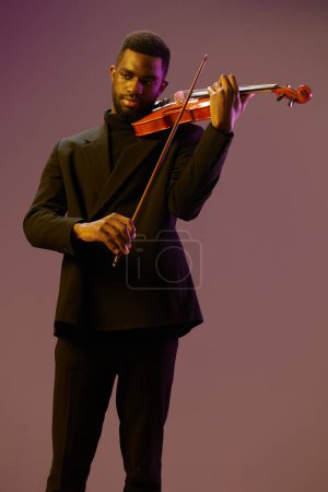 Foto de Elegante hombre de traje negro tocando violín sobre fondo violeta vibrante en imagen de concepto de performance artística - Imagen libre de derechos