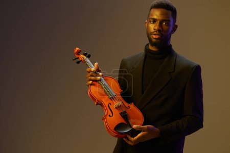 Photo for Elegant man in black suit with violin in front of light brown background, musical instrument concept - Royalty Free Image