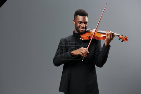 Young African American man in black suit playing violin on grey background in a captivating musical performance portrait