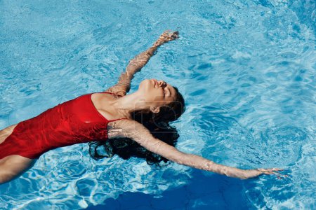 Foto de Mujer feliz nadando en la piscina en traje de baño rojo con el pelo largo suelto, protección de la piel con protector solar, concepto de relajarse en vacaciones. Foto de alta calidad - Imagen libre de derechos