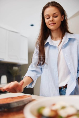 Foto de Mujer de camisa azul preparando comida en plato en la cocina en casa, cocina y concepto de estilo de vida - Imagen libre de derechos