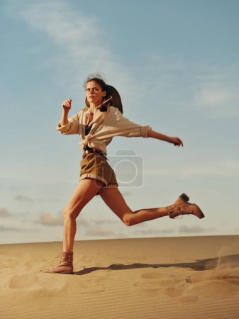 Téléchargez les photos : Joyeux jeune femme courant les bras tendus dans le désert sous le soleil éclatant - en image libre de droit