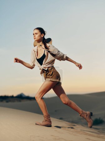 Foto de Mujer corriendo a través de dunas de arena del desierto con sombrero y mochila, disfrutando de aventura al aire libre y libertad - Imagen libre de derechos
