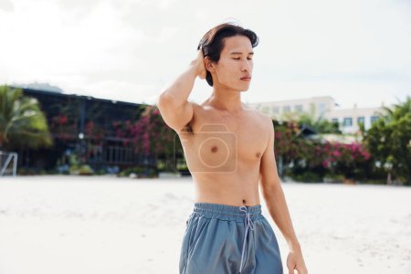 Téléchargez les photos : Homme Asiatique Musclé Profitant de Vacances Tropical Beach, Souriant sous les Palmiers - en image libre de droit