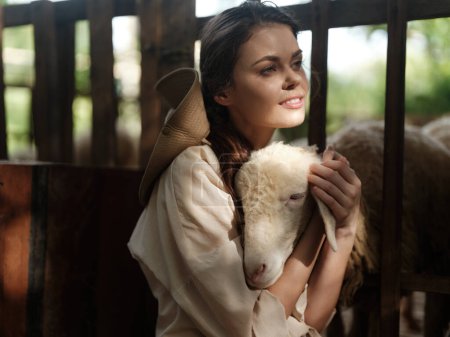 Téléchargez les photos : Une femme tient un agneau dans ses bras alors qu'elle se tient devant une clôture - en image libre de droit