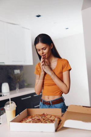 Téléchargez les photos : Une femme priant devant une boîte de pizza et un verre de lait Pensée spirituelle et gourmandise dans la nourriture réconfortante - en image libre de droit