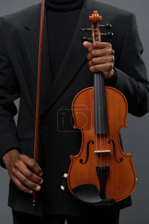 Photo for African American man holding violin in front of black background, showcasing musical talent and passion - Royalty Free Image