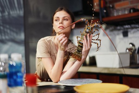 Téléchargez les photos : Femme tenant un homard à une table de cuisine, se préparant à un délicieux concept de repas de fruits de mer - en image libre de droit