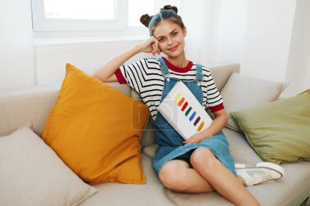 Téléchargez les photos : Happy Teenage Girl, une artiste créative, Peindre un portrait mignon sur un canapé à la maison - en image libre de droit