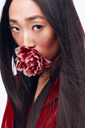 Foto de Hermosa mujer con el pelo largo negro sosteniendo flor en frente de la cara con la boca abierta por sorpresa - Imagen libre de derechos
