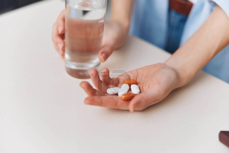 Foto de Persona sosteniendo un frasco de pastillas y un vaso de agua junto a otro frasco de pastillas en una mesa - Imagen libre de derechos