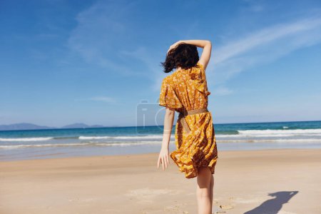Femme en robe jaune debout sur la plage avec le dos à l'océan profiter moment paisible au bord de l'eau