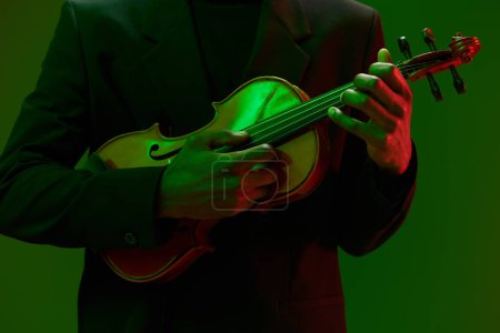 Foto de Elegante hombre de traje tocando el violín con dramática iluminación verde y roja en el fondo - Imagen libre de derechos