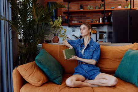 Junge Frau genießt einen friedlichen Moment auf einer gemütlichen orangefarbenen Couch mit Buch und Kaffeetasse