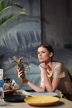 The woman enjoying a meal with a lobster and plate of food at a table in restaurant
