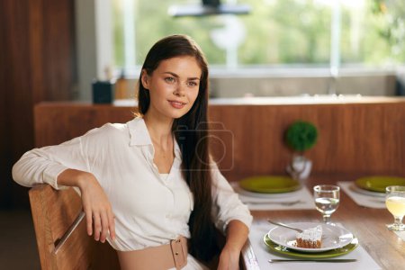Photo for Romantic Dinner Date at Home Smiling Woman Enjoying a Delicious Meal at Trendy Dining Table The elegant and ecstatic brunette sits at a beautifully set table, adorned with a homemade cake and a glass - Royalty Free Image